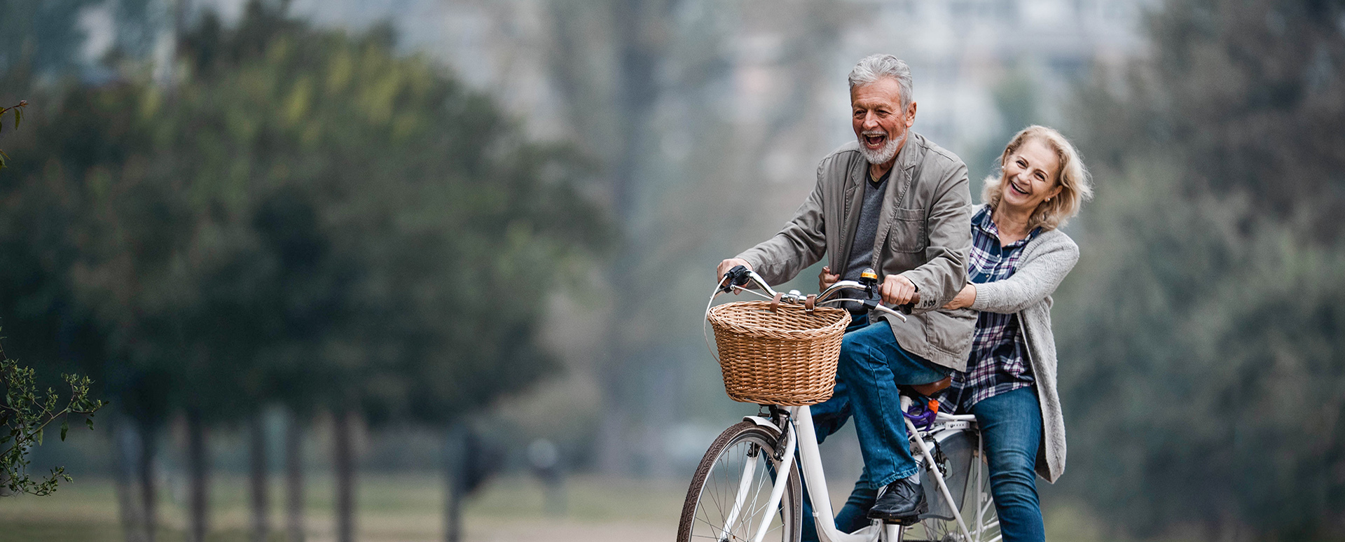 Happy mature couple having fun on a bicycle in autumn day at the park.