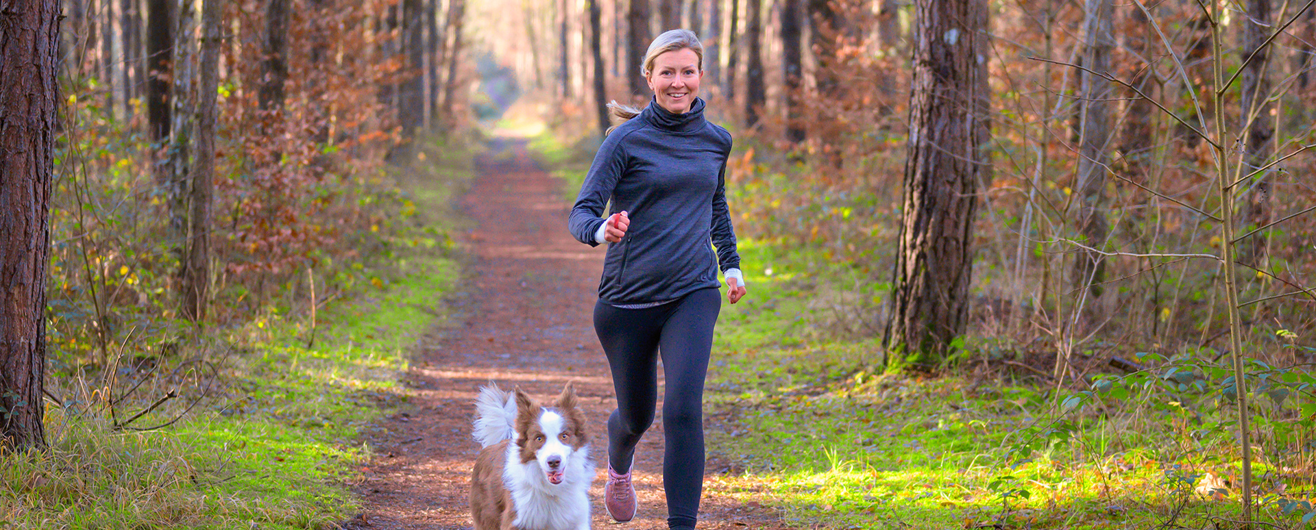 older woamn running in woods with dog